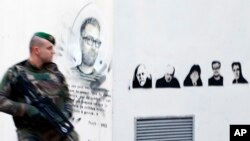 Un soldat français à côté des portraits des caricaturistes tués, Charb, Honoré, Wolinski, Cabu et Tignous, à l'extérieur de l'ancien bureau du journal satirique Charlie Hebdo à Paris, un an après les attaques, 7 janvier 2016.