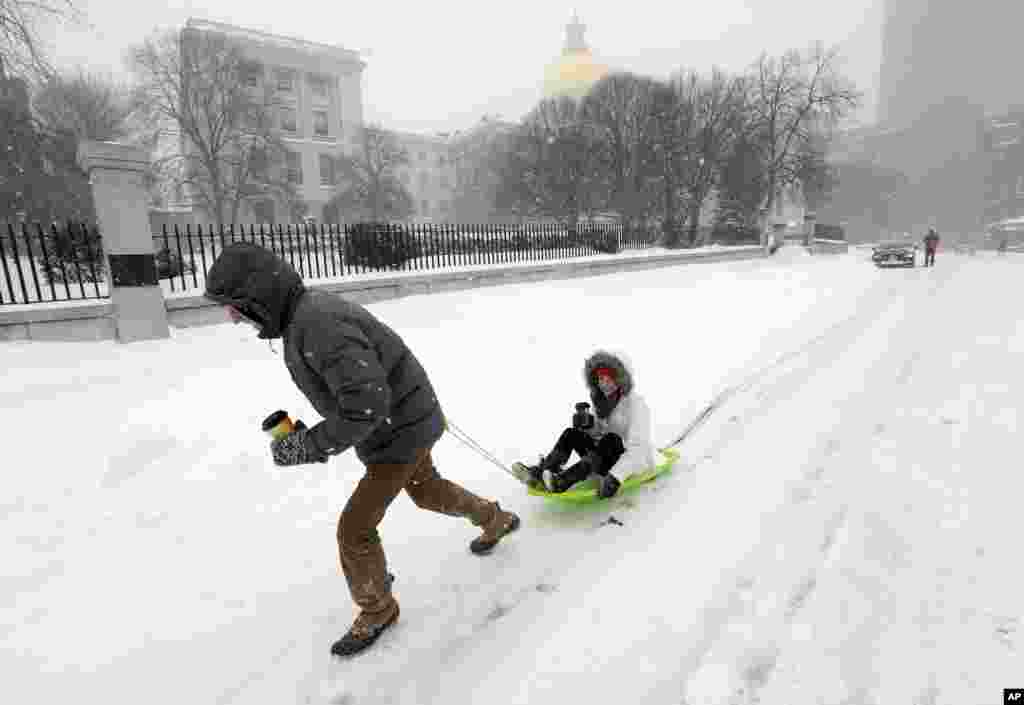 John Joy pulls his girlfriend Brooke Finan past the Statehouse after they made a search for coffee during a winter snowstorm in Boston, Massachusetts, Jan. 27, 2015.