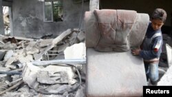 Un garçon retire une chaise des décombres d'un immeuble après un raid aérien dans la ville de Mesraba, un bastion rebelle à l'est de la capitale Damas, en Syrie, le 26 novembre 2017.
