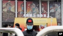 世界衛生組織團隊於 2021年1月30日星期六抵達中中國中部湖北省武漢市舉行的抗擊冠狀病毒展覽後，一名戴著口罩和帶有中國國旗的帽子的保安人員守衛入口。