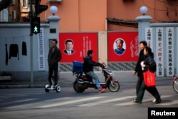 FILE PHOTO: People cross a street in front of posters depicting late Chairman Mao Zedong (R) and China's President Xi Jinping in Shanghai, China, March 1, 2016.