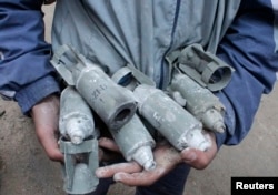 FILE - A boy holds unexploded cluster bombs after jet shelling by forces loyal to Syria's President Bashar al-Assad in the al-Meyasar district of Aleppo February 21, 2013.