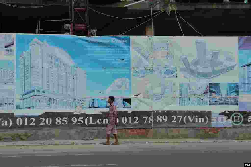 បុរសម្នាក់ដើរកាត់ផ្ទាំងផ្សាយពាណិជ្ជកម្មអំពីគម្រោងទីក្រុង Olympia City នៅក្បែរការដ្ឋានសំណង់អគារមួយនៅថ្ងៃទី២៩ ខែកញ្ញា ឆ្នាំ២០១៤។ (នូវ ពៅលក្ខិណាVOA)