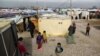 FILE - Syrian refugees stand outside their tents, during the visit of Filippo Grandi, the United Nations High Commissioner for Refugees, UNHCR, to a camp in the town of Saadnayel, in the Bekaa valley, Lebanon, Jan. 22, 2016. 