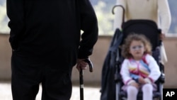 Un homme âgé utilise une canne pour soutenir sa marche. Il s’approche d’un enfant dans une poussette, Rome, Italie, le 27 Avril 2007. 
