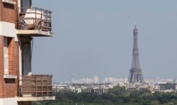 A woman enjoys the sun on her balcony as the Eiffel Tower is clearly seen in the background during the nationwide confinement to counter the conoravirus in Saint-Cloud, west of Paris, April 22, 2020.