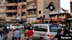 សមាជិក​ក្រុម Islamic State in Iraq and the Levant (ISIL) គ្រវី​ទង់ ISIL ខណៈ​ដែល​ពួក​គេ​​បើក​រថយន្ត​ក្នុង​ក្រុង Raqqa ប្រទេស​អ៊ិរ៉ាក់​កាល​ពី​ថ្ងៃ​ទី​២៩​ខែ​មិថុនា​ឆ្នាំ​២០១៤។