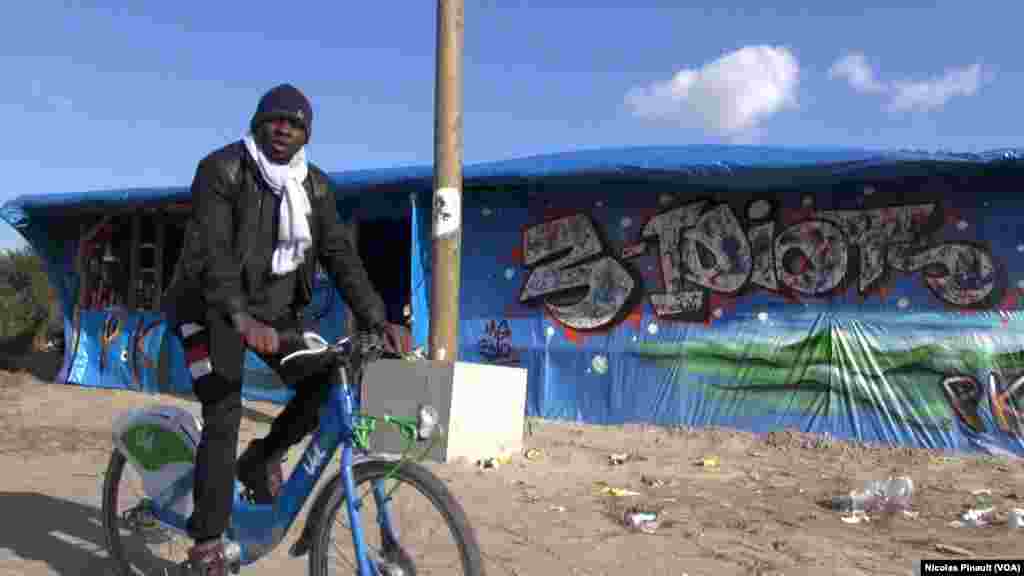 Un migrant fait du vélo dans la "jungle" qui est le nom du camp situé aux abords de Calais dans le nord de la France, 13 octobre 2015 (Nicolas Pinault/VOA). 