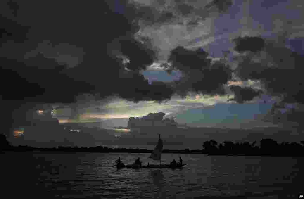 Flood affected villagers travel on a boat as monsoon clouds surround the flood affected Gagalmari village in Assam state, India, July 2, 2012.