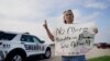 Seorang warga bernama Mary Ann Foley membawa poster berisi seruan protes untuk pihak berwenang agar segera mengambil tindakan untuk menhentikan penembakan massal ketika ia mengunjungi acara mengenang korban penembakan di Allen, Texas, pada 7 Mei 2023. (Foto: AP/LM Otero)