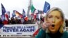 A person holds a mask of France's National Front (FN) defeated presidential candidate, Marine Le Pen, as people gather with French and European flags near the Eiffel Tower and a banner with the message, "France tells Hate: Never Again" the day after presi