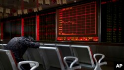 FILE - An investor takes a nap in front of an electronic board displaying stock prices at a brokerage house in Beijing, Monday, Sept. 17, 2018.