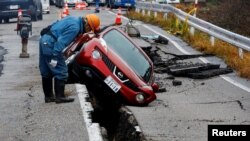 2024年1月3日，日本赤水附近，一名工人查看一辆在地震后被困在道路裂缝中的汽车。（路透社照片）