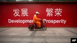 北京一位保潔員騎著電動車經過一面牆，牆上的宣傳標語分別用中、英文寫著“發展 繁榮。（美聯社照片）
