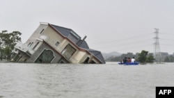 中國江西省上饒市鄱陽湖附近地區被洪水淹沒，幾人劃著小船經過一所被洪水沖倒的民宅。 （2020年7月15日）