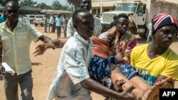 Des hommes portent une femme qui s'est évanouie pendant un échange des tirs à Baya Dombia, Bangui, RCA,13 décembre 2015.