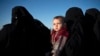 Seorang wanita menggendong seorang anak saat dia menunggu untuk diperiksa Pasukan Demokratik Suriah (SDF) yang didukung AS di gurun di luar Baghouz, Suriah, 1 Maret 2019. (Foto: AP)