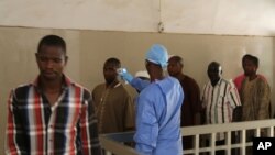 Un aide soignant, au centre, prend la température à un patient à l'hôpital gouvernemental Ignace Deen à Conakry, Guinée, le 18 mars 2016.