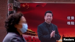 一位戴口罩的婦女從習近平的宣傳畫前走過（2020年3月12號）。