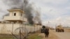 FILE - A member of the Afghan security forces walks as smoke billows from a building after a Taliban attack in Gereshk district of Helmand province, Afghanistan, March 9, 2016.